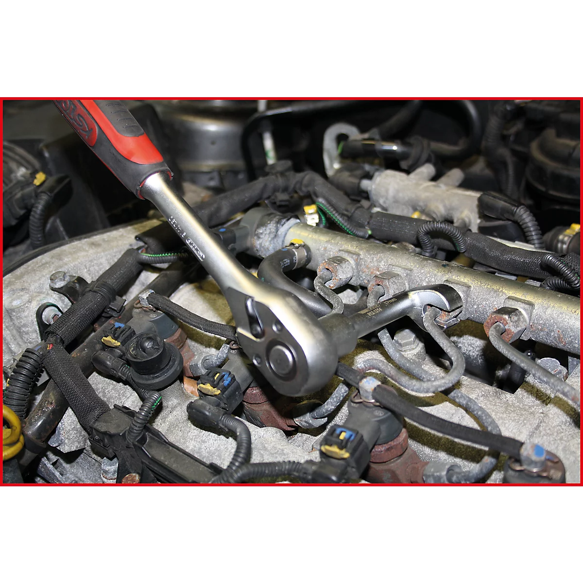 Eine Hand hält eine Ratsche, die an einem Motor arbeitet. Kabel und Rohre umgeben die Ratsche.